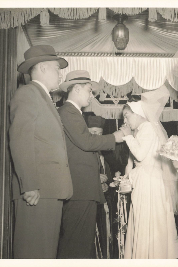 Husband and wife underneath a Chupah with the Rabbi. The Bride is about to drink the wine from underneath her veil.